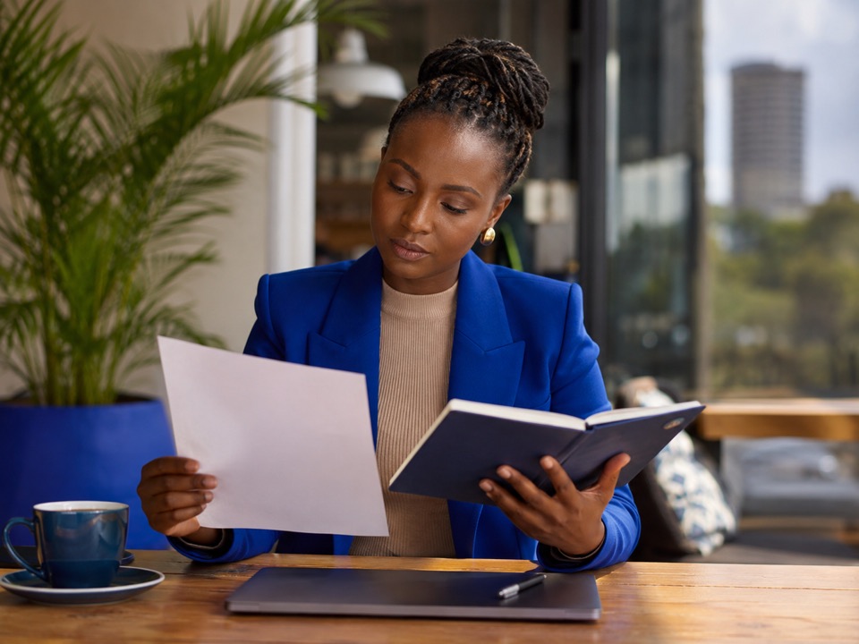 Illustration of a woman reviewing a document and notebook at her desk.