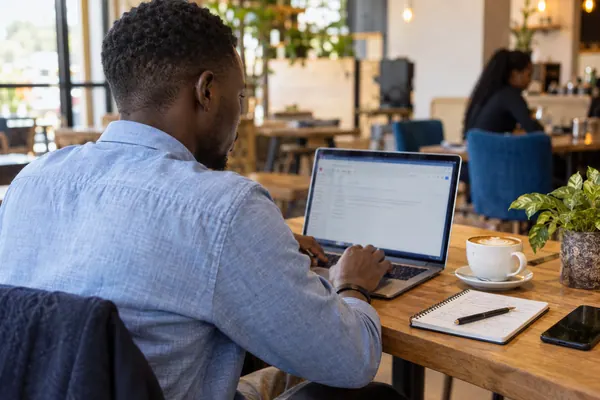 A young man writing an application email on a laptop in a cafe